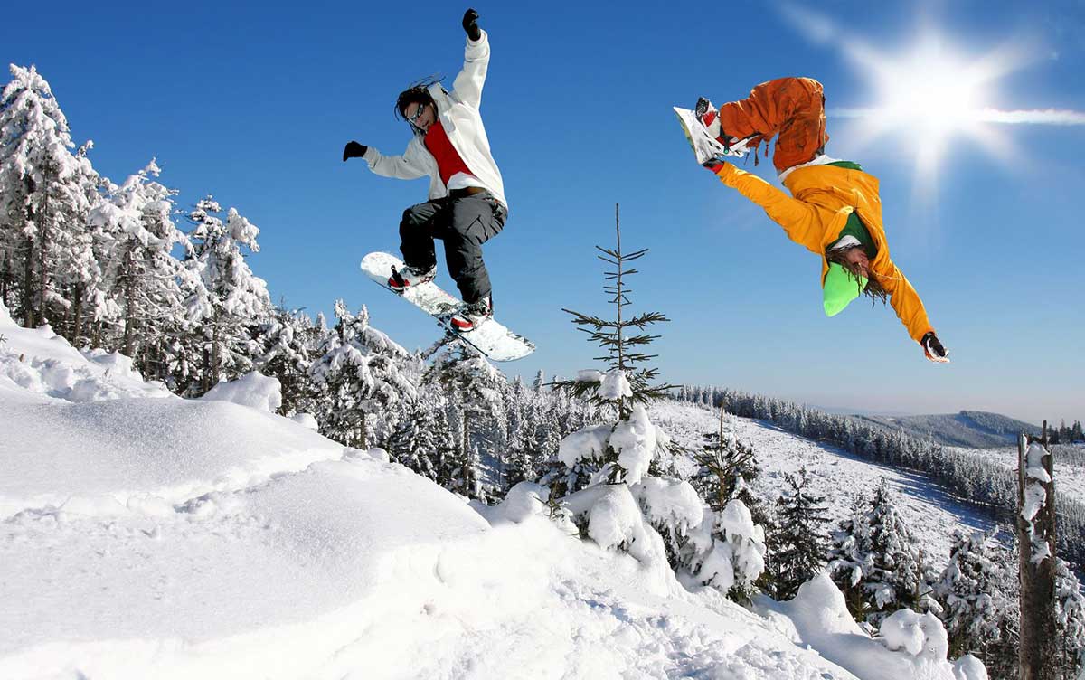 Two people performing snowboarding tricks on a snowy mountain